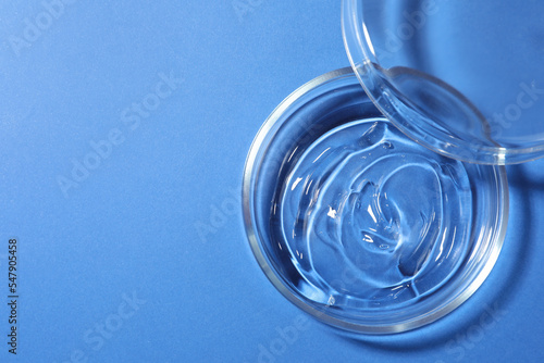 Petri dish with liquid and lid on blue background, flat lay. Space for text