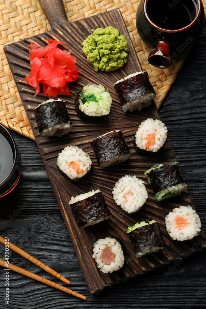 Tasty sushi rolls served on black wooden table, flat lay