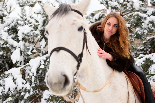 Focus on a girl riding a white horse. A winter walk in a coniferous forest