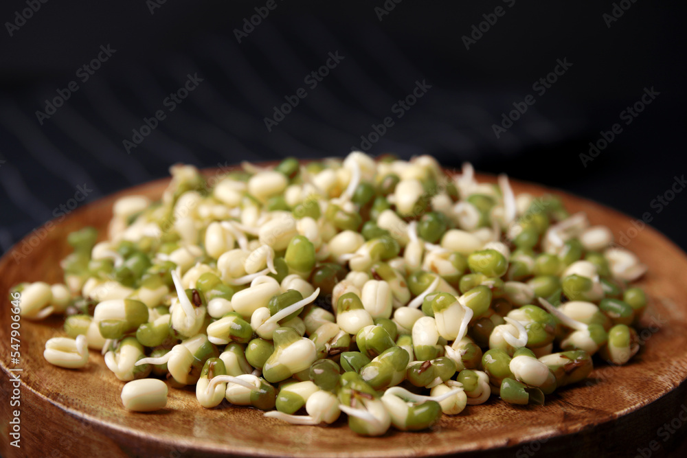 Wooden plate with sprouted green mung beans on dark background, closeup Wooden plate with sprouted green mung beans on dark background, closeup