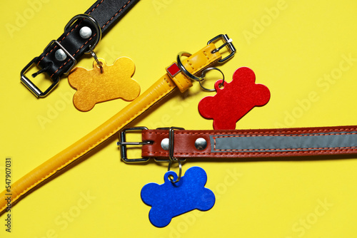 Color leather dog collars with tags in shape of bone on yellow background, flat lay