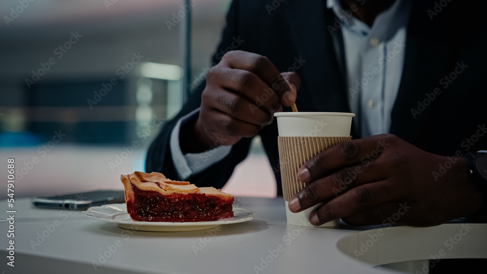 Unrecognizable African man worker businessman in formal suit sitting at table in cafe cafeteria restaurant stirs sugar in cup of aromatic coffee tea latte cappuccino drink prepare eat cherry cake pie Unrecognizable African man worker businessman in formal suit sitting at table in cafe cafeteria restaurant stirs sugar in cup of aromatic coffee tea latte cappuccino drink prepare eat cherry cake pie