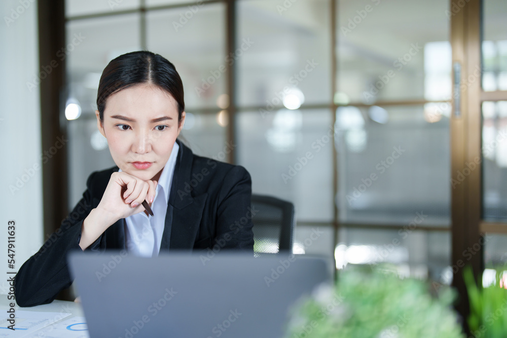 Portrait of a thoughtful Asian businesswoman looking at financial statements and making marketing plans using a computer on her desk Portrait of a thoughtful Asian businesswoman looking at financial statements and making marketing plans using a computer on her desk