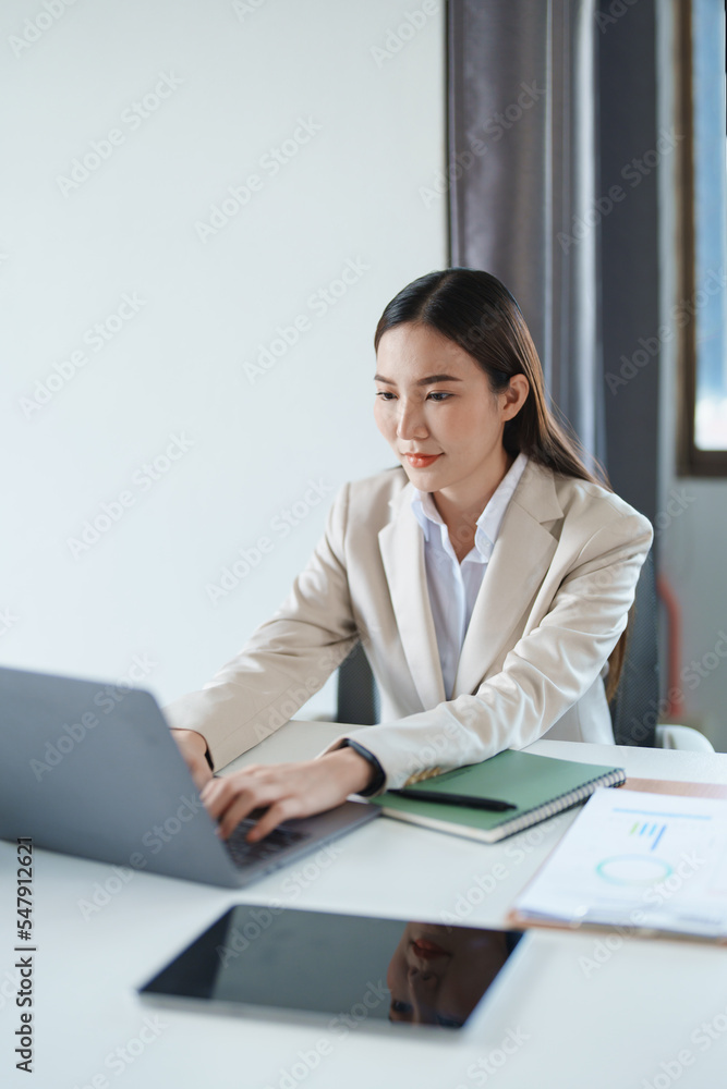 Portrait of a young Asian woman showing a smiling face as she using computer and financial documents on her desk in the early morning hours. Portrait of a young Asian woman showing a smiling face as she using computer and financial documents on her desk in the early morning hours.