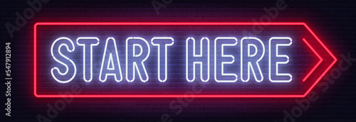 Start here neon sign on brick wall background.