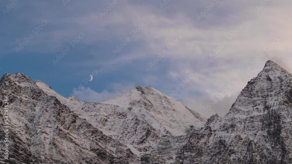 Zoom in timelapse of sunset over snow covered Himalayan mountains with moon moving in cloudy sky at Lahaul, Himachal Pradesh, India. Evening sunset sky timelapse at snow mountain during winter. Zoom in timelapse of sunset over snow covered Himalayan mountains with moon moving in cloudy sky at Lahaul, Himachal Pradesh, India. Evening sunset sky timelapse at snow mountain during winter.