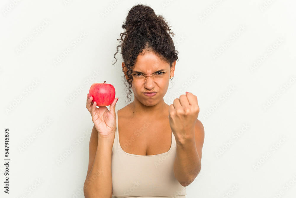 Young brazilian woman holding a red apple isolated showing fist to camera, aggressive facial expression. Young brazilian woman holding a red apple isolated showing fist to camera, aggressive facial expression.