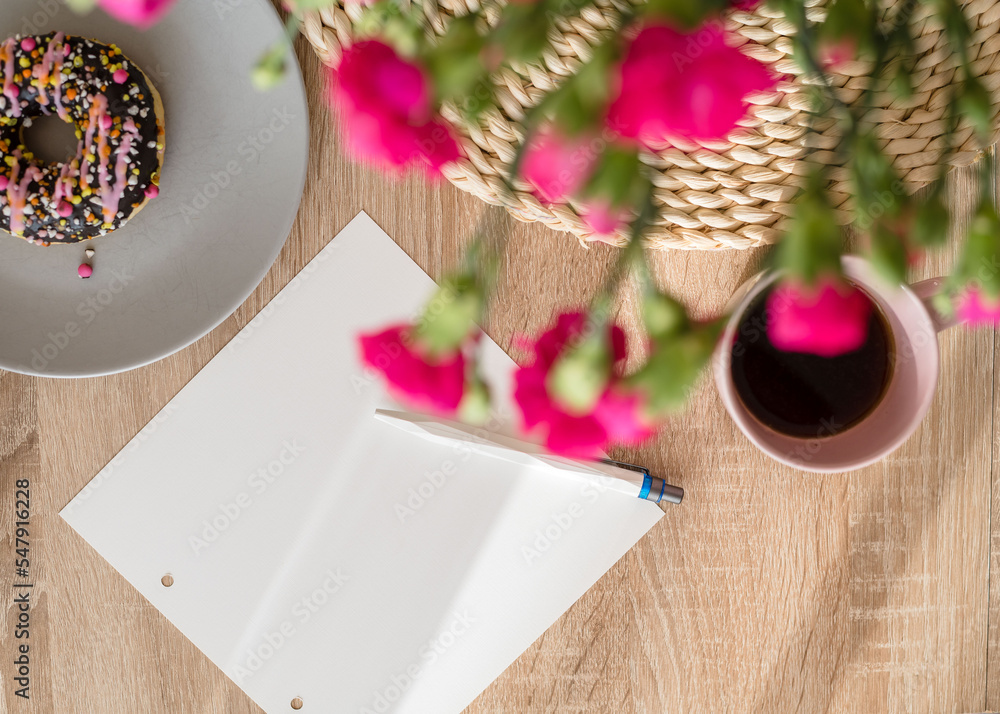 Cozy breakfast and planning. Notepad and pen, cup of coffee, pink donut, flowers and candles on the table. Women's desktop. Top view Cozy breakfast and planning. Notepad and pen, cup of coffee, pink donut, flowers and candles on the table. Women's desktop. Top view