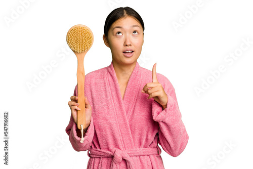 Young asian woman holding a shower brush isolated pointing upside with opened mouth.