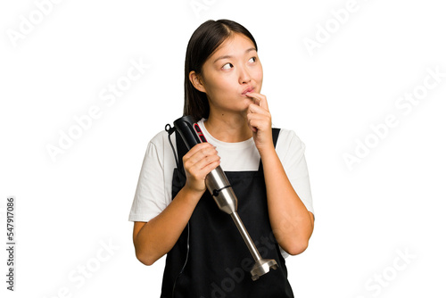 Young asian cook woman holding a blender isolated looking sideways with doubtful and skeptical expression.