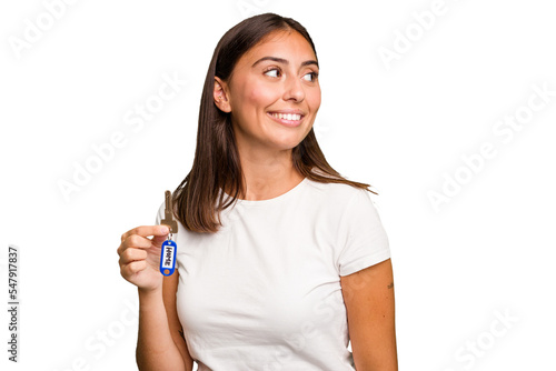 Young caucasian woman holding a home keys isolated looks aside smiling, cheerful and pleasant.