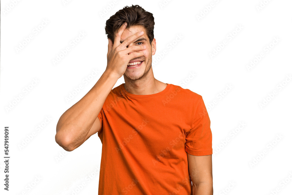 Young caucasian handsome man isolated blink at the camera through fingers, embarrassed covering face. Young caucasian handsome man isolated blink at the camera through fingers, embarrassed covering face.