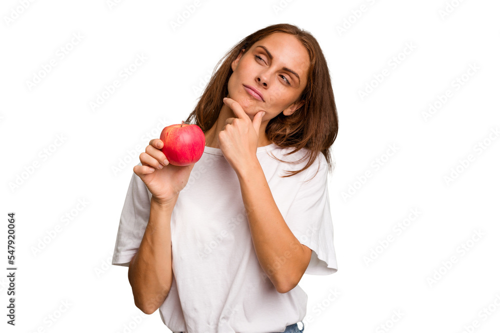 Young caucasian woman holding a red apple isolated looking sideways with doubtful and skeptical expression. Young caucasian woman holding a red apple isolated looking sideways with doubtful and skeptical expression.