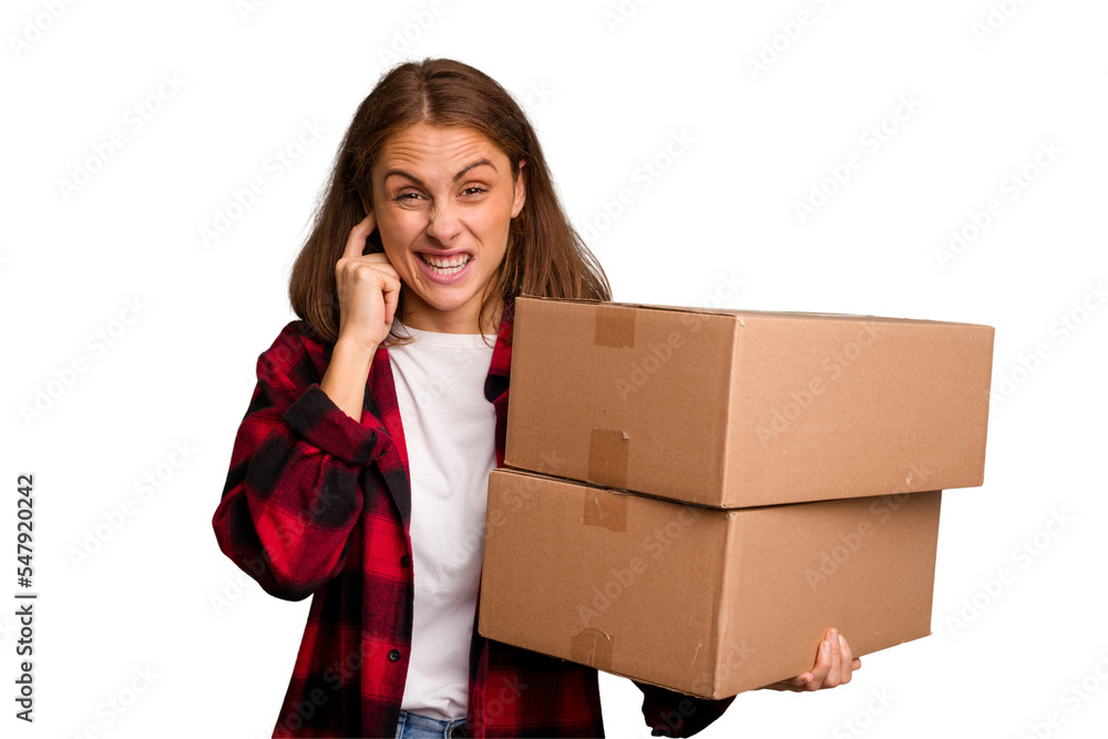 Young caucasian woman moving while picking up a box full of things isolated covering ears with hands. Young caucasian woman moving while picking up a box full of things isolated covering ears with hands.