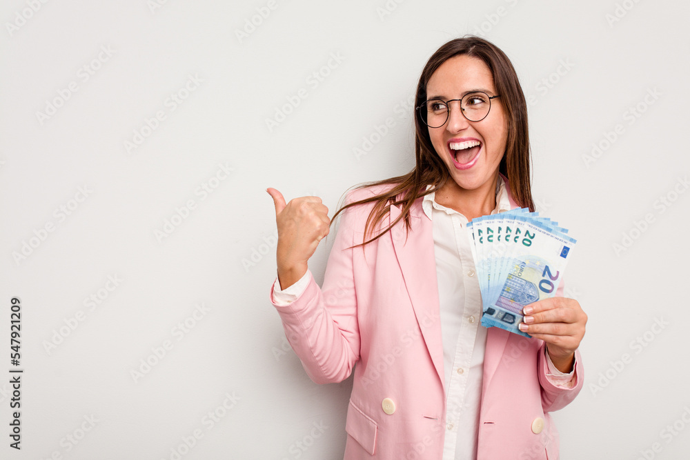 Business caucasian woman holding banknotes isolated on white background points with thumb finger away, laughing and carefree. Business caucasian woman holding banknotes isolated on white background points with thumb finger away, laughing and carefree.
