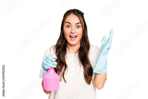 Young cleaner caucasian woman isolated on green chroma background receiving a pleasant surprise, excited and raising hands.