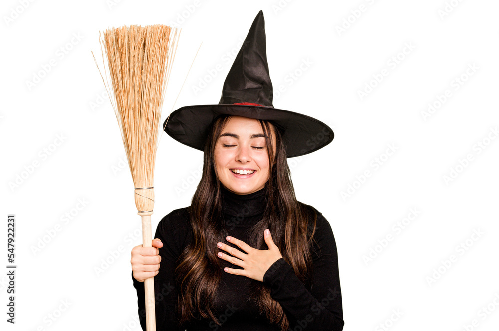 Young caucasian woman dressed as a witch holding a broom isolated on green chroma background laughs out loudly keeping hand on chest. Young caucasian woman dressed as a witch holding a broom isolated on green chroma background laughs out loudly keeping hand on chest.