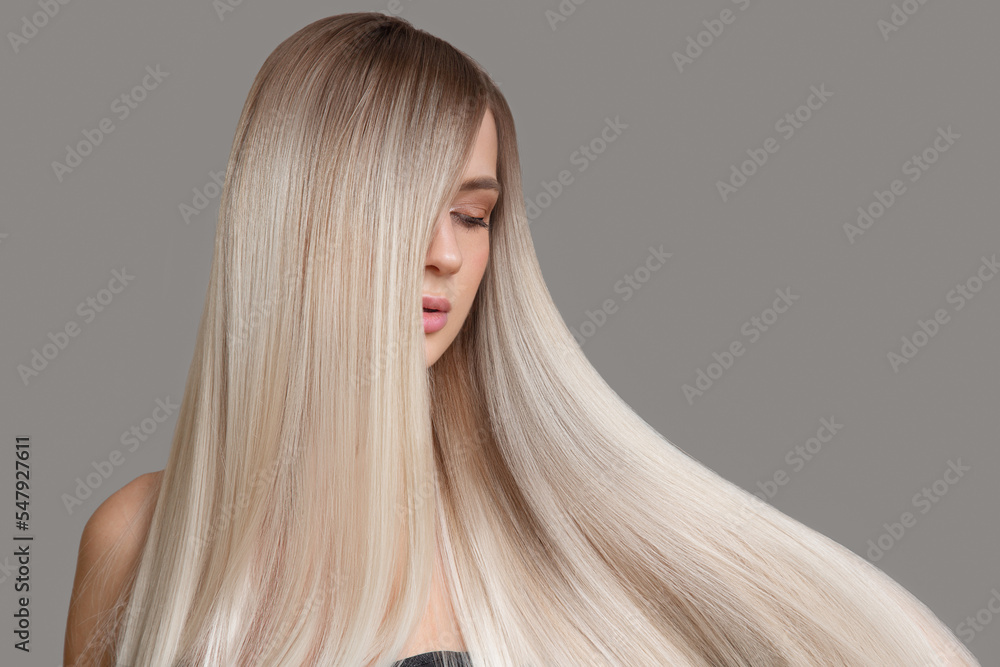 Beautiful young blonde with straight shiny hair. Portrait on a gray background. Hair and makeup - obrazy, fototapety, plakaty 