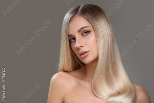 Beautiful young blonde with straight shiny hair. Portrait on a gray background. Hair and makeup photo