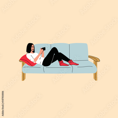 Woman sitting on sofa holds smartphone in her hand. Casual lady and browsing social media on mobile device. Girl on couch uses phone for chatting and surfing internet