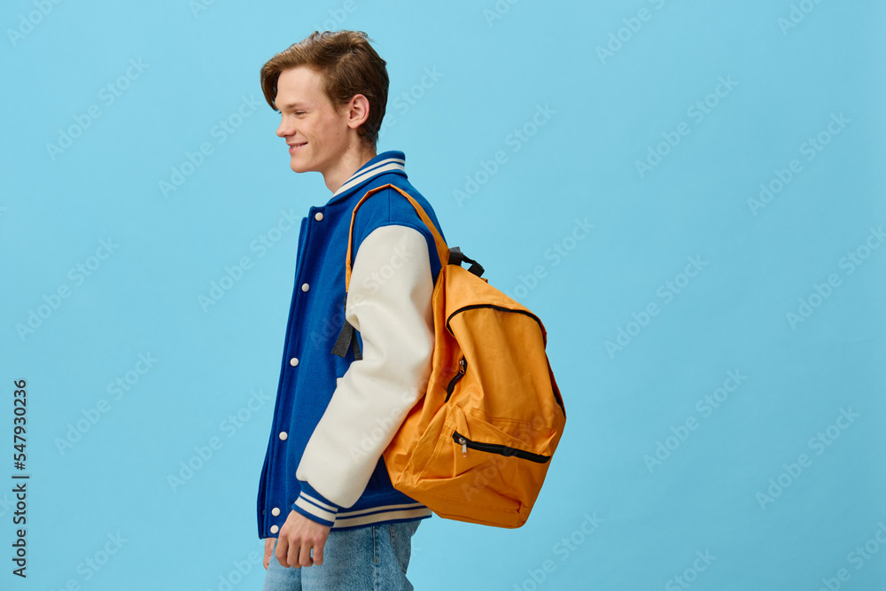 student with a backpack on his shoulder posing on a blue background student with a backpack on his shoulder posing on a blue background