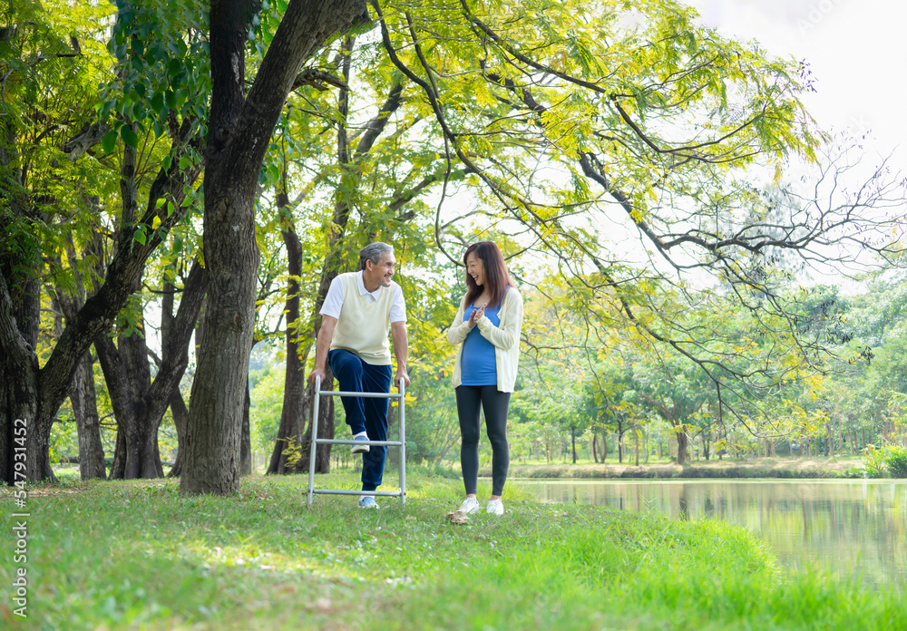 father practices walking with walker and exercise legs,a daughter encourage beside him at the park,concept for elderly people exercise, rehabilitation, relaxing wellness, family relationship father practices walking with walker and exercise legs,a daughter encourage beside him at the park,concept for elderly people exercise, rehabilitation, relaxing wellness, family relationship