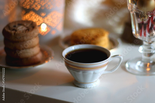 Glass with Christmas ornaments, cup of tea, cookies, candles and knitted blanket by the fireplace. Cozy Christmas at home.