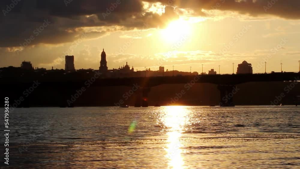 Silhouette of evening city sinking into darkness. A capital of Ukraine Kyiv panoramic view of a bridge, water in Dnipro river, buildings against yellow sunset sky. Lights out in a metropolis, blackout Silhouette of evening city sinking into darkness. A capital of Ukraine Kyiv panoramic view of a bridge, water in Dnipro river, buildings against yellow sunset sky. Lights out in a metropolis, blackout