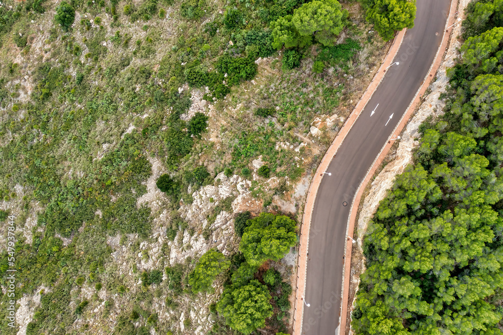 Aerial view of mountain road passing through the green forest and along a mountain