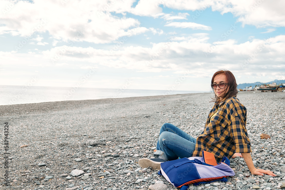 Woman in warm plaid shirt resting and watching sea on winter beach. Traveling. Wellbeing and harmony concept. Unity with nature.
