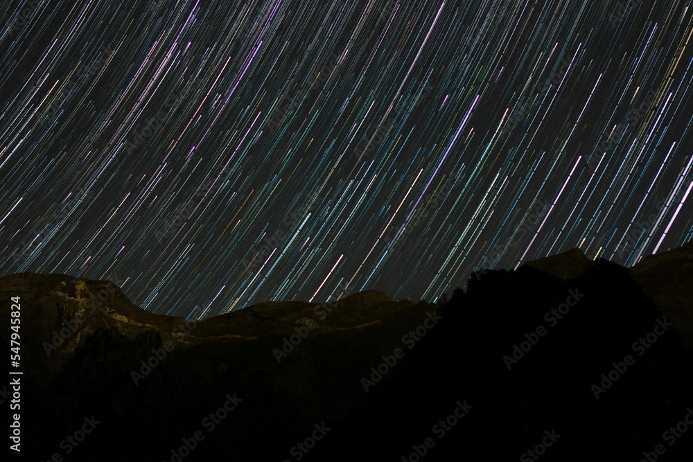 Star trails in the black night sky over the land silhouette, long ...