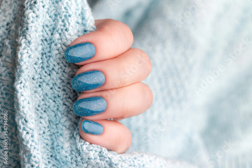 Female hand in blue knitted sweater with beautiful holiday manicure - blue glitter nails. Nail care concept © MariiaDemchenko