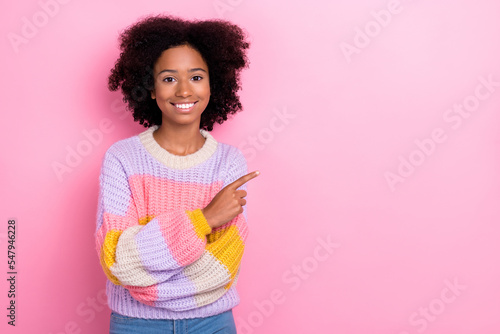 Photo of toothy beaming optimistic girl with perming coiffure wear knit sweater indicating empty space isolated on pink color background