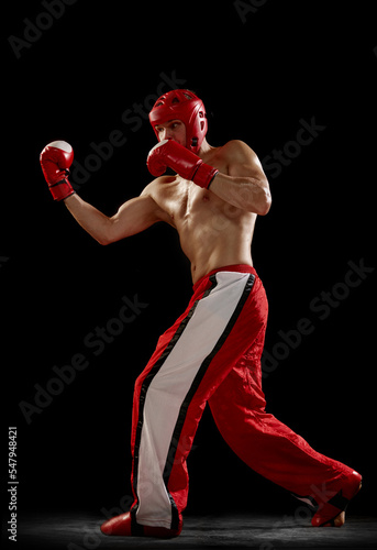 Studio shot of male kickboxer, mma fighter in motion and action isolated over dark background. Muay thai. Sport, competition, energy, combat sports. Red and black © master1305