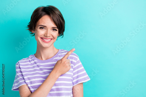 Portrait of optimistic adorable nice cheerful girl dressed striped t-shirt directing empty space isolated on teal color background
