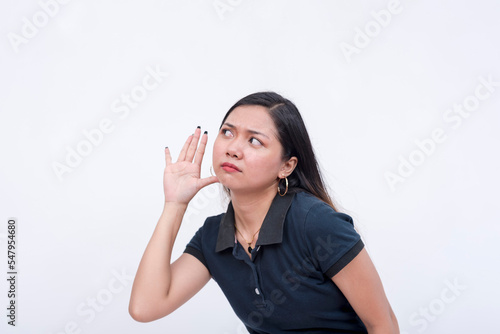 A snoopy young woman eavesdropping on a private conversation. Bending to the left, hands on her ear. Isolated on a white background. photo