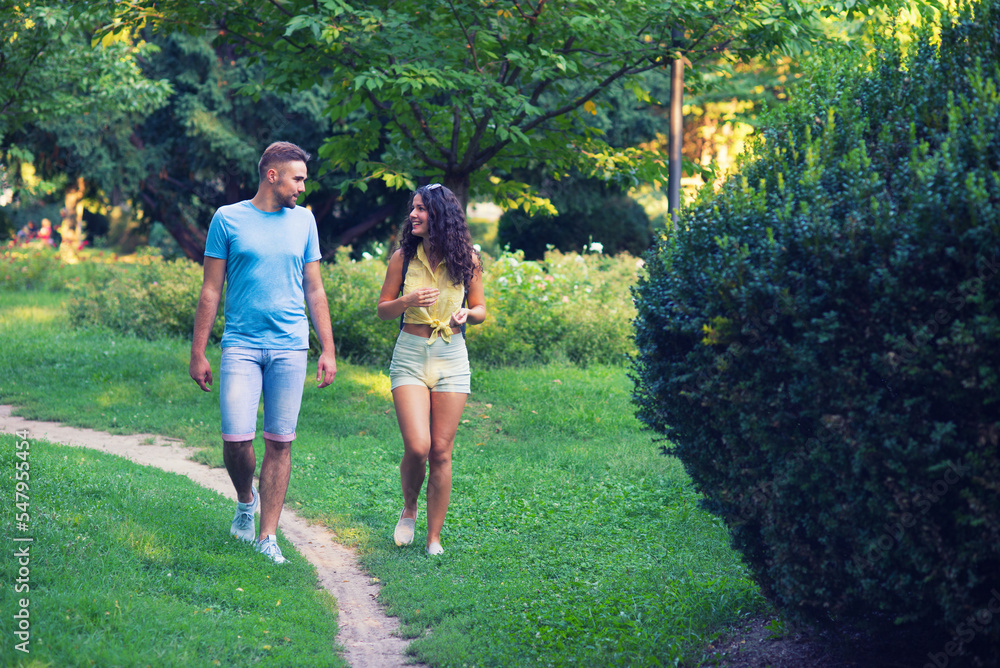 Fototapeta premium Young smiling couple walking down the footpath in the summer park