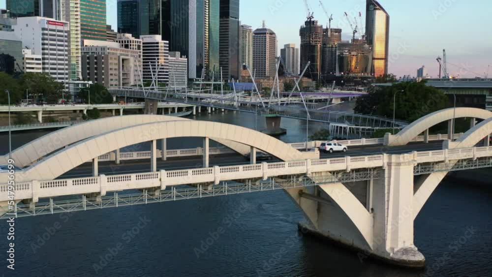 Cinematic flyover downtown cityscape with high rise buildings and skyscrapers along the riverside at Brisbane city, central business district and traffic crossing on William Jolly Bridge at sunset. Cinematic flyover downtown cityscape with high rise buildings and skyscrapers along the riverside at Brisbane city, central business district and traffic crossing on William Jolly Bridge at sunset.