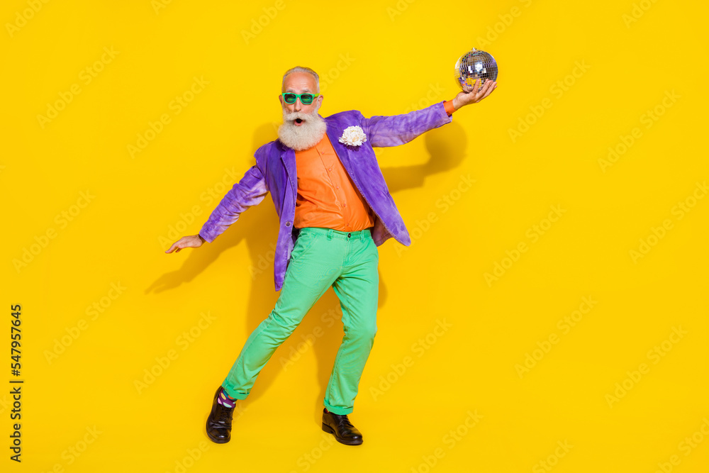 Full length photo of aged showman arm hold glowing disco ball clubbing isolated on yellow color background Full length photo of aged showman arm hold glowing disco ball clubbing isolated on yellow color background