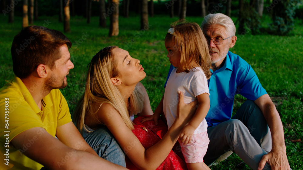 Fototapeta premium Pretty little girl and her parents together with grandfather have a lovely family time together in the middle of the park they enjoy the time together