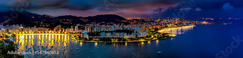 Panoramic photograph of the shore of Guanabara Bay in Rio de Janeiro at night with the buildings and citylights in Botafogo and Flamengo neighborhoods and the hills in the background