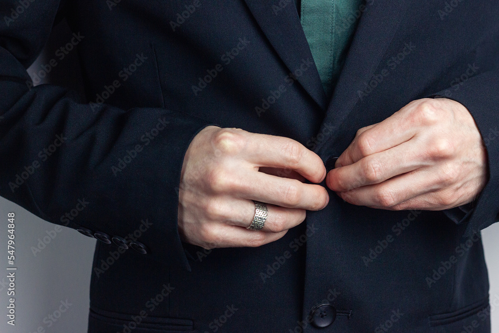 Obraz premium Male hands of a businessman in a business suit with a ring on his finger fasten a button on a jacket. Horizontal orientation photo, business style.