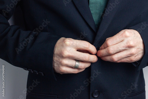 Male hands of a businessman in a business suit with a ring on his finger fasten a button on a jacket. Horizontal orientation photo, business style.