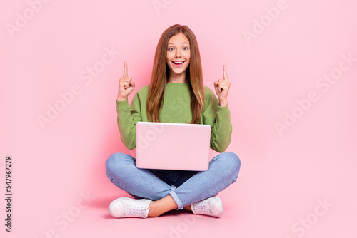 Full length photo of cute excited school girl dressed sweatshirt pointing empty space working modern device isolated pink color background © deagreez