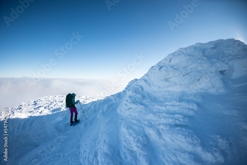 A woman with a backpack in snowshoes climbs a snowy mountain