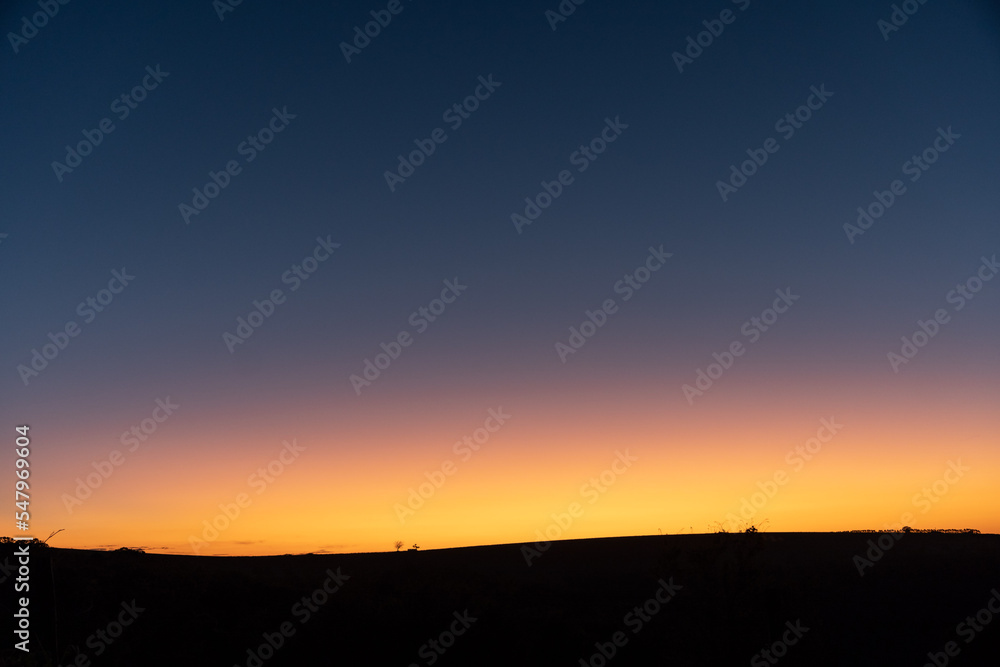 Fototapeta premium Background with landscape of an amazing and illuminated orange sunset in the blue sky, with a black base