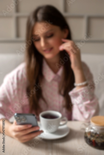 defocused and blurry woman drink tea in cafe searching for information in phone in lunch time. vertical photo