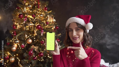 Woman in red sweater and Santa's hat holding a mobile phone with a green screen