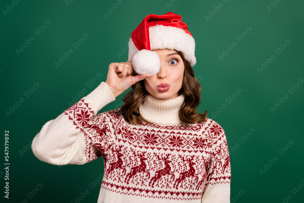 Photo of charming lady pouted lips kiss arm hold headwear pompom ball cover eye isolated on green color background Photo of charming lady pouted lips kiss arm hold headwear pompom ball cover eye isolated on green color background