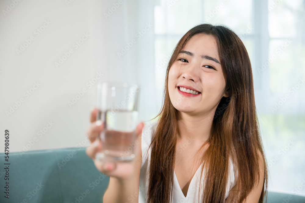 Portrait of Asian young woman holding drinking nature water on hand at home, Happy smiling female beauty with water glass for drink in living room, Healthy lifestyle Portrait of Asian young woman holding drinking nature water on hand at home, Happy smiling female beauty with water glass for drink in living room, Healthy lifestyle